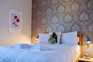 A neatly made bed with white linens and two pillows, a framed botanical illustration on the wall, and a lamp on the nightstand. - Sophisticated Edinburgh Apartment in City Centre (Edinburgh)
