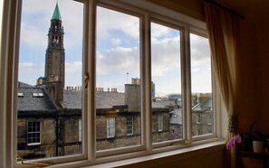 A room with a large window overlooking a historic building with a tower and multiple chimneys. - Sophisticated Edinburgh Apartment in City Centre (Edinburgh)