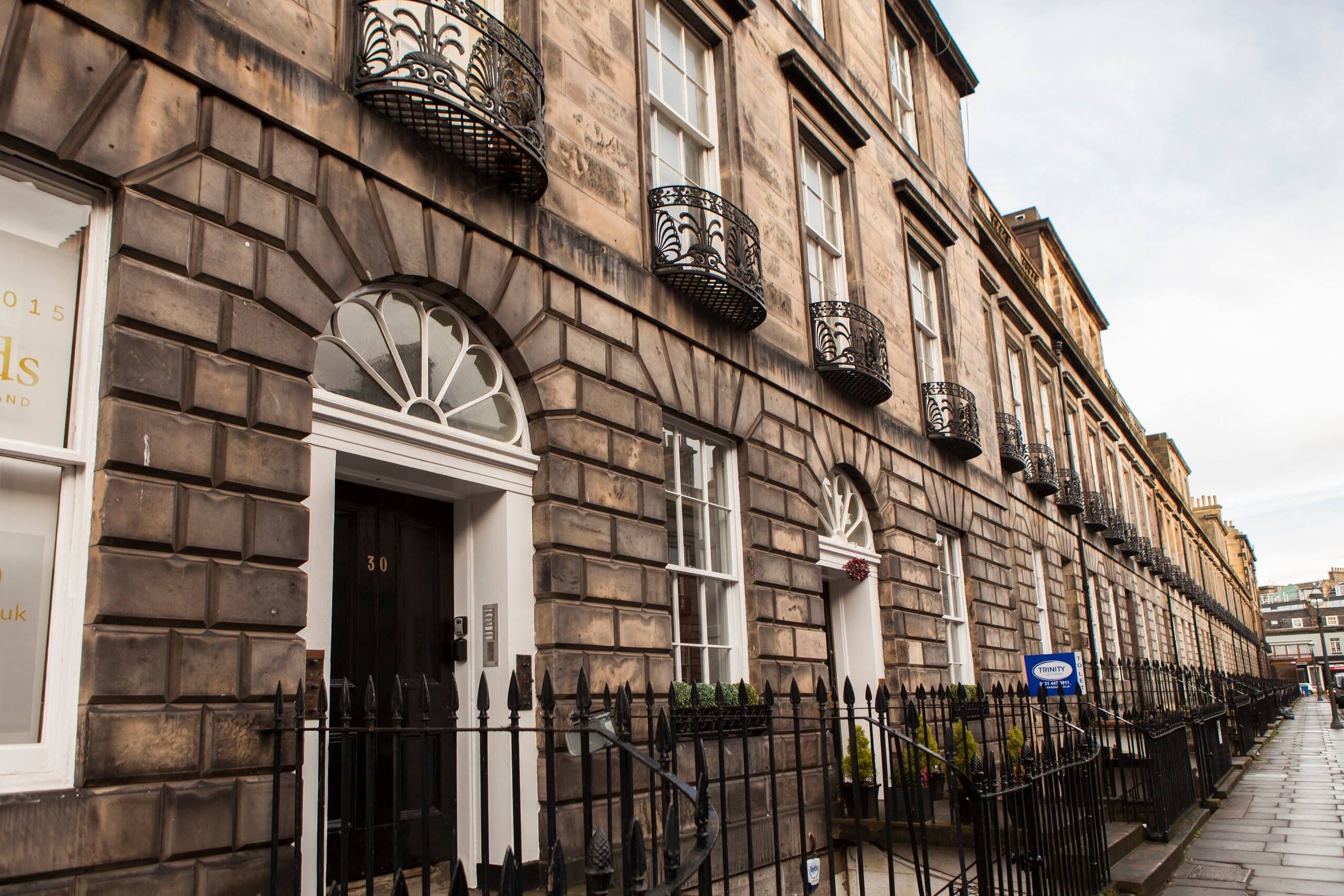 A row of traditional stone buildings with ornate iron balconies and a clear sky.