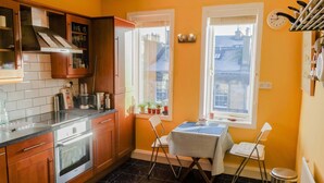 A compact kitchen with wooden cabinets, a built-in oven, a dining table with chairs, and two windows providing natural light. - Sophisticated Edinburgh Apartment in City Centre (Edinburgh)