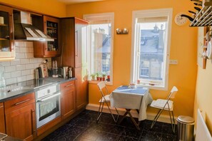 A compact kitchen with wooden cabinets, a built-in oven, a dining table with chairs, and two windows providing natural light. - Sophisticated Edinburgh Apartment in City Centre (Edinburgh)