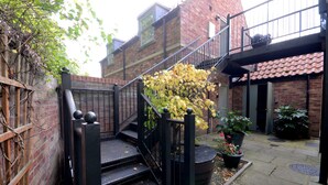 Un bâtiment en briques avec un escalier menant à un deuxième étage, entouré de plantes en pot et d’un petit jardin.