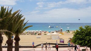 A beach scene with palm trees, beach umbrellas, and people. - Front line beach apartment with wifi and air conditioning (Arona)
