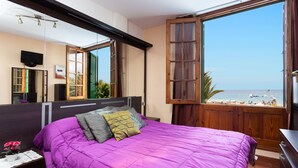 A bedroom with a large bed, a wooden headboard, a TV, and a window with a view of the beach. - Front line beach apartment with wifi and air conditioning (Arona)