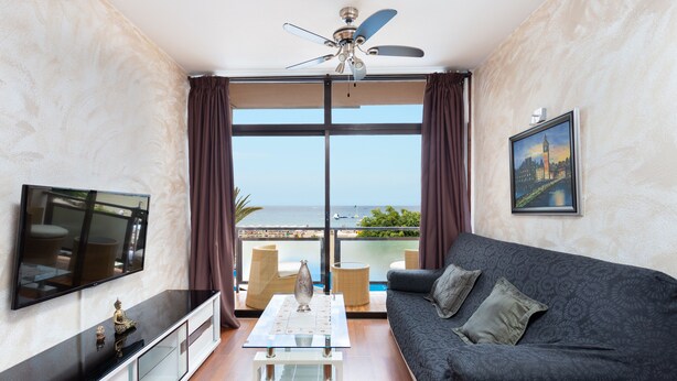 A living room with a sofa, a coffee table, a TV, and a balcony with a view of the sea. - Front line beach apartment with wifi and air conditioning (Arona)