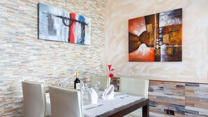 A dining area with a brick wall, two abstract paintings, a wooden table, and white upholstered chairs. - Front line beach apartment with wifi and air conditioning (Arona)