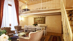 Ein geräumiges Wohnzimmer mit hoher Decke, einem Essbereich mit Glastisch und einer Treppe, die zu einer oberen Etage führt.