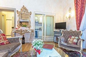 Ein Wohnzimmer mit Sofa, Sessel, einem Tisch mit Blumenvase, einer Flasche und einem Fernseher.
