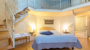 Ein Schlafzimmer mit Bett, Nachttisch, Lampe, Gemälde, Treppe und Tür.