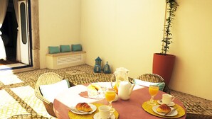 A breakfast table set with croissants, coffee, and orange juice, surrounded by wicker chairs and a potted plant. - Renovated apartment with private exterior in the center of Setúbal (Setúbal)