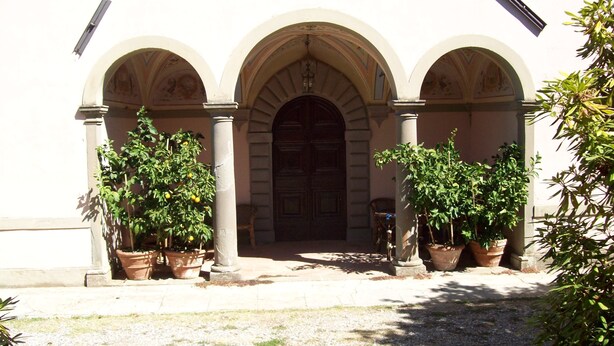 A building with a central entrance flanked by three arches, a dark wooden door, and potted plants on either side. - Noble villa for 16 people, with park and pool in Tuscany  (Nocchi)