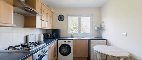 Une cuisine compacte équipée d’une cuisinière à gaz, d’un four, d’un lave-linge et d’une petite table.