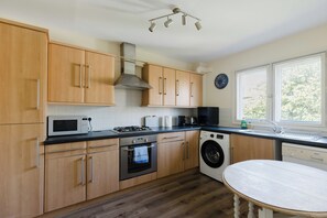 A modern kitchen with wooden cabinets, a microwave, stove, oven, and a washing machine. - Bright 1 BDR Apartment with Private Terrace (London)