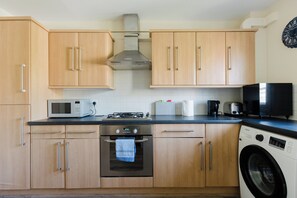 Una cocina moderna con armarios de madera, microondas, horno, lavadora y cafetera.