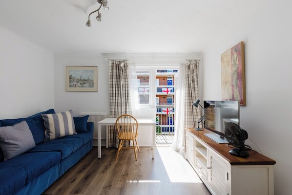 A living room with a blue sofa, a wooden chair, a white table, and a TV on a wooden cabinet.