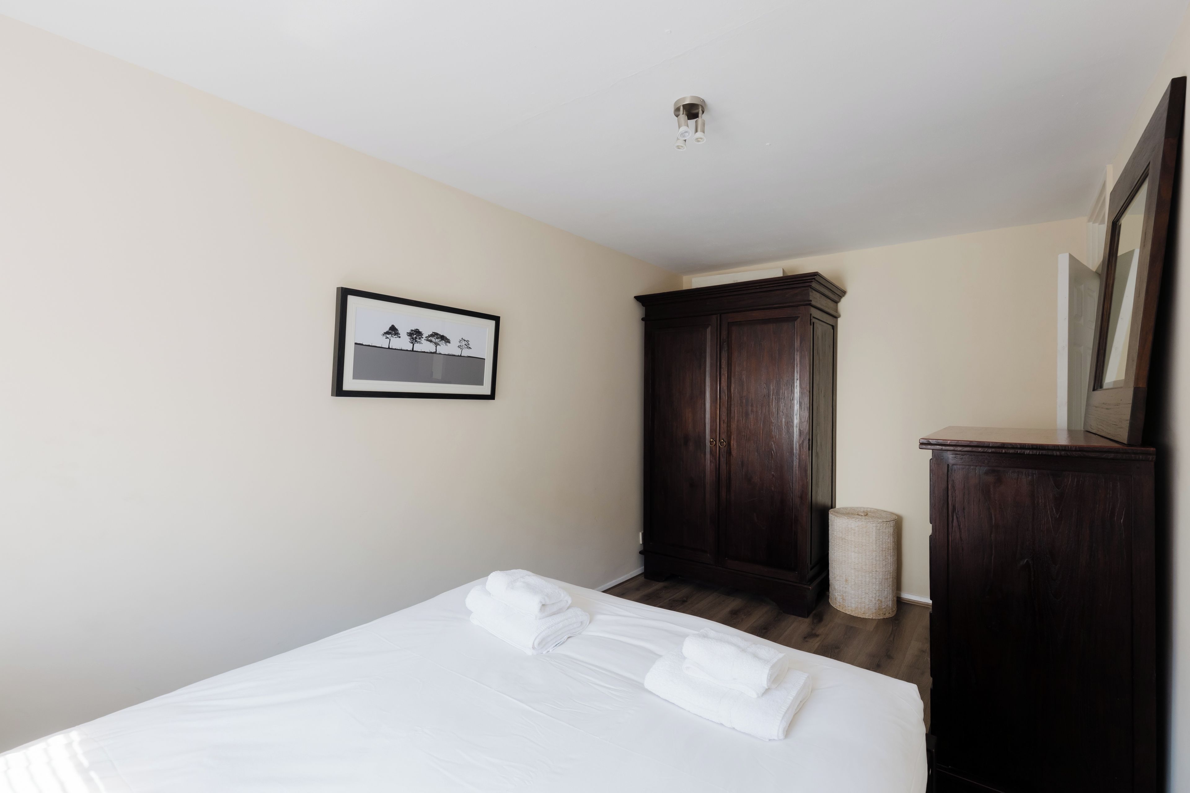 A hotel room with a bed, a framed picture on the wall, a dark wooden wardrobe, and a mirror.