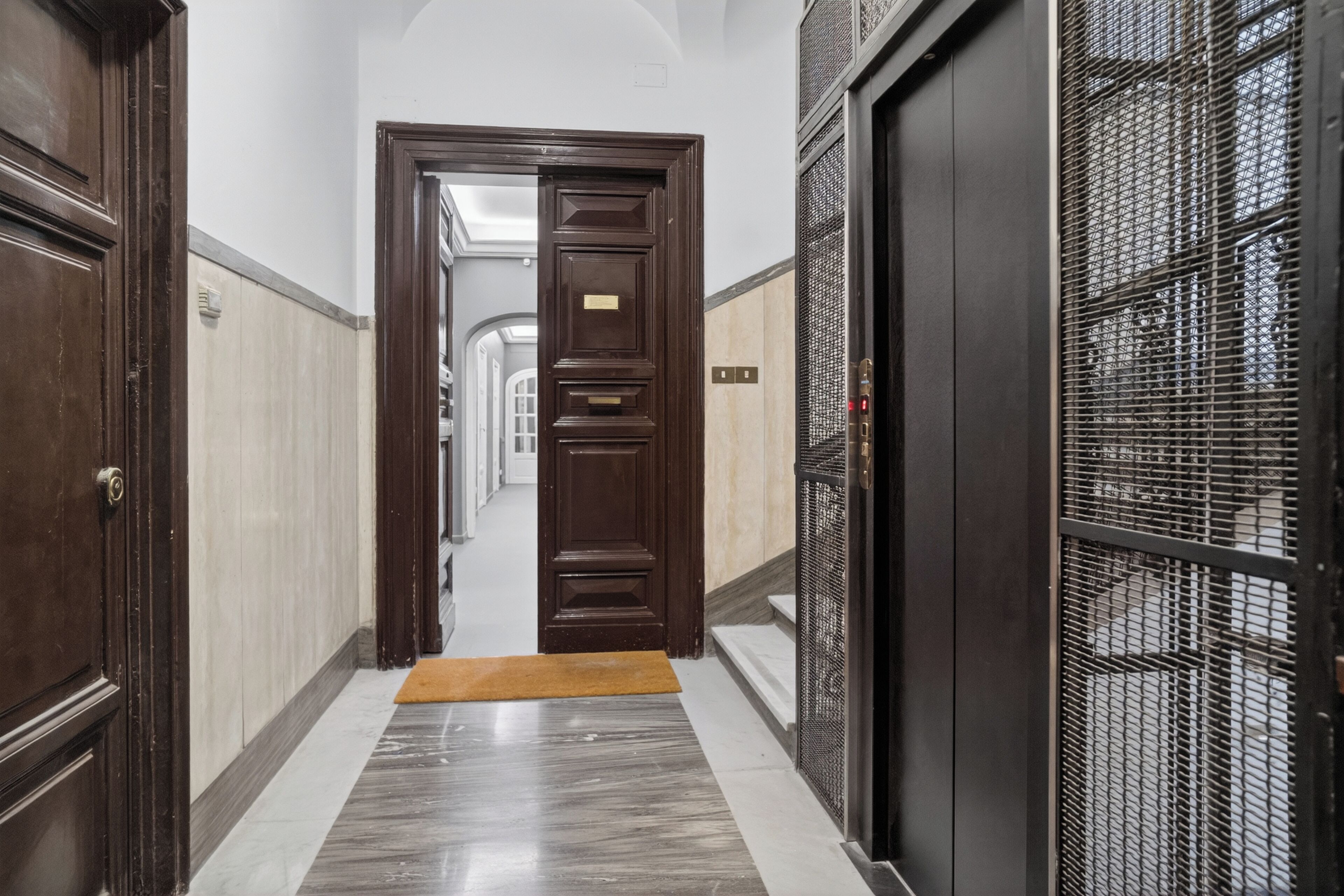 Un pasillo con puerta de madera, reja metálica y suelo de mármol.