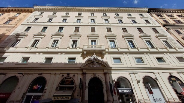 A multi-story building with a classical facade, featuring a central entrance with a decorative archway and a sign above it.