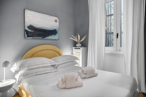 A neatly made bed with white linens, a bedside lamp, and a wall-mounted abstract painting.