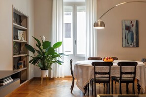 A dining area with a round table, chairs, a potted plant, and a painting on the wall.
