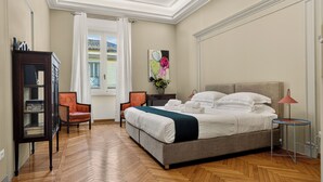 A hotel room with a large bed, a desk, a chair, a bookshelf, and a window with curtains.