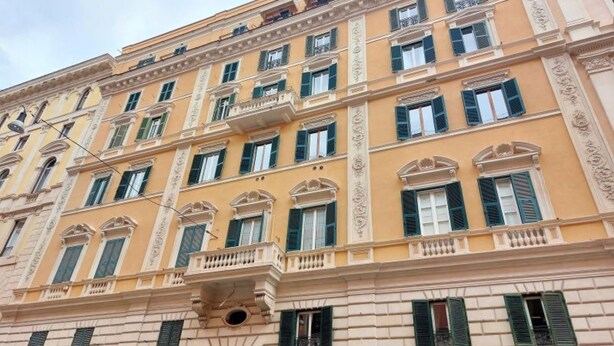 Un edificio de varios pisos con fachada amarilla, contraventanas verdes y detalles arquitectónicos de estilo clásico.