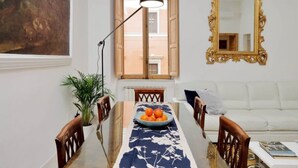 Un comedor con una mesa, sillas, un cuenco de fruta, una lámpara de pie, un espejo y un sofá blanco.