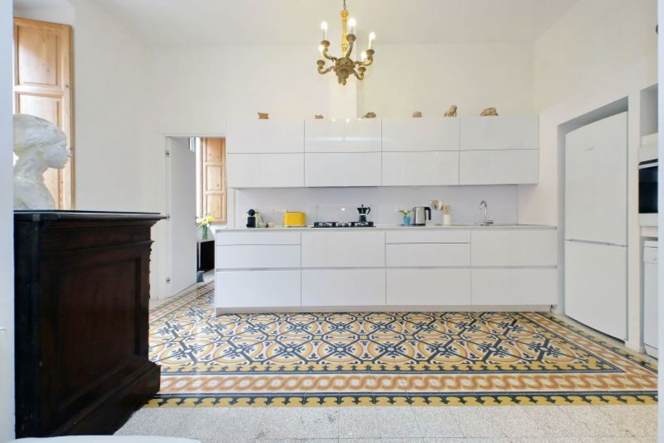 A modern kitchen with white cabinets, a patterned tile floor, and a chandelier.
