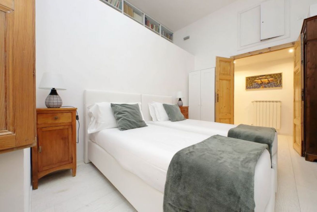 A bedroom with a large bed, bedside tables, a wardrobe, and a door leading to another room.