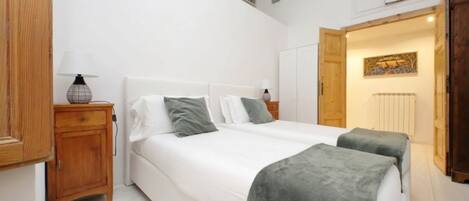 A bedroom with a large bed, bedside tables, a wardrobe, and a door leading to another room.
