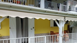 Un bâtiment jaune avec un balcon dont la rambarde est blanche, un patio couvert et une porte.