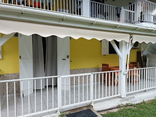Un edificio amarillo con barandal blanco, un patio cubierto y una puerta.