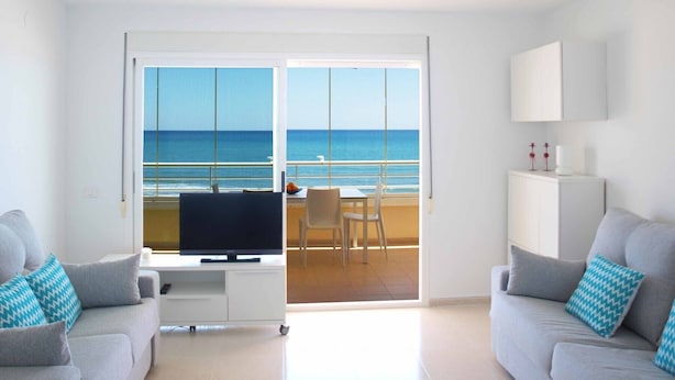 Un salon moderne comprenant un téléviseur, deux canapés, un coin repas et un balcon avec vue sur la mer.