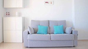 Un canapé gris avec deux coussins à motifs, un meuble blanc et un thermostat fixé au mur.