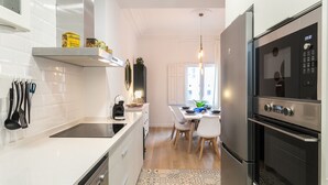 Eine moderne Küche mit weißen Schränken, einem Edelstahlkühlschrank und einem Essbereich mit einem gemusterten Teppich.