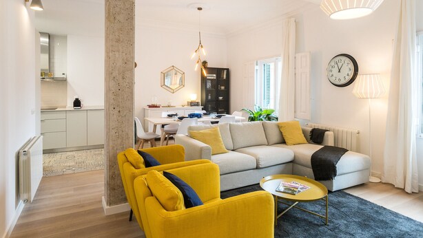 Ein modernes Wohnzimmer mit einer Couch, gelben Sessel, einem Couchtisch und einem Essbereich mit Tisch und Stühlen.