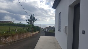Une rue étroite, avec un bâtiment blanc sur le côté droit, une clôture en bois et, au loin, une vue sur la mer.