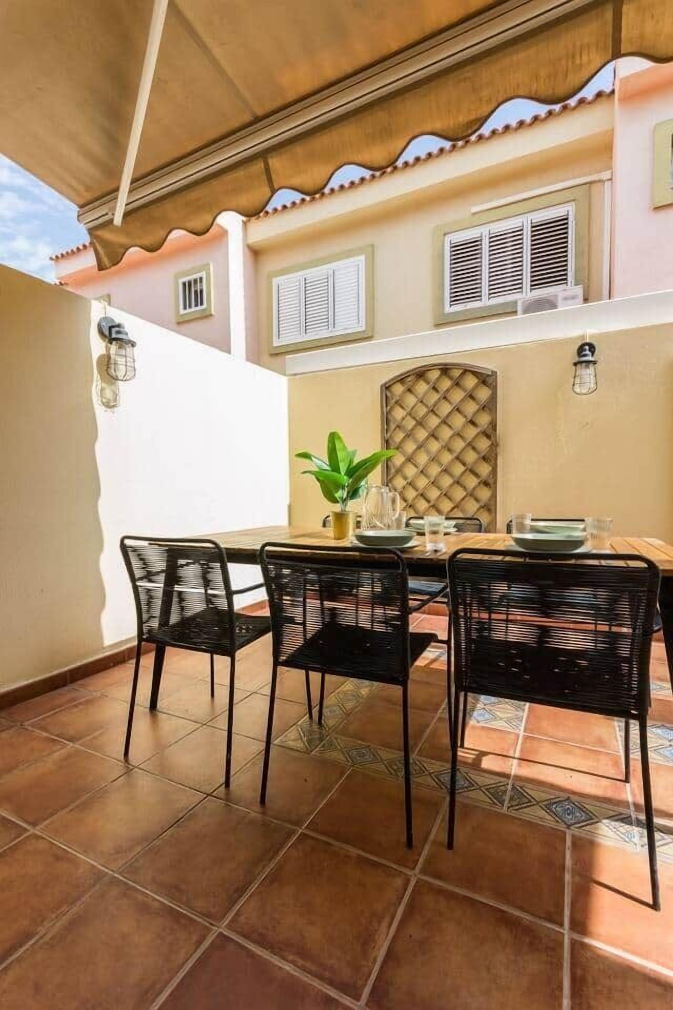An outdoor dining area with a table and chairs, a potted plant, and a decorative wall panel.