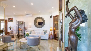 A spacious living room with a white sofa, grey armchairs, and a glass coffee table. A large mirror and a bronze statue are also visible. - Atticus Luxury Penthouse with Stunning Terrace  (Roma)
