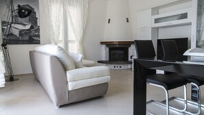 Een moderne woonkamer met een witte bank, een zwarte eettafel en een open haard.