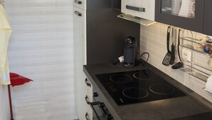 Een moderne keuken met witte kasten, een zwart aanrecht, een ingebouwde oven en een paarse hanglamp.