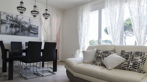 Een moderne woonkamer met een beige bank, zwarte stoelen, een eettafel en een kroonluchter.