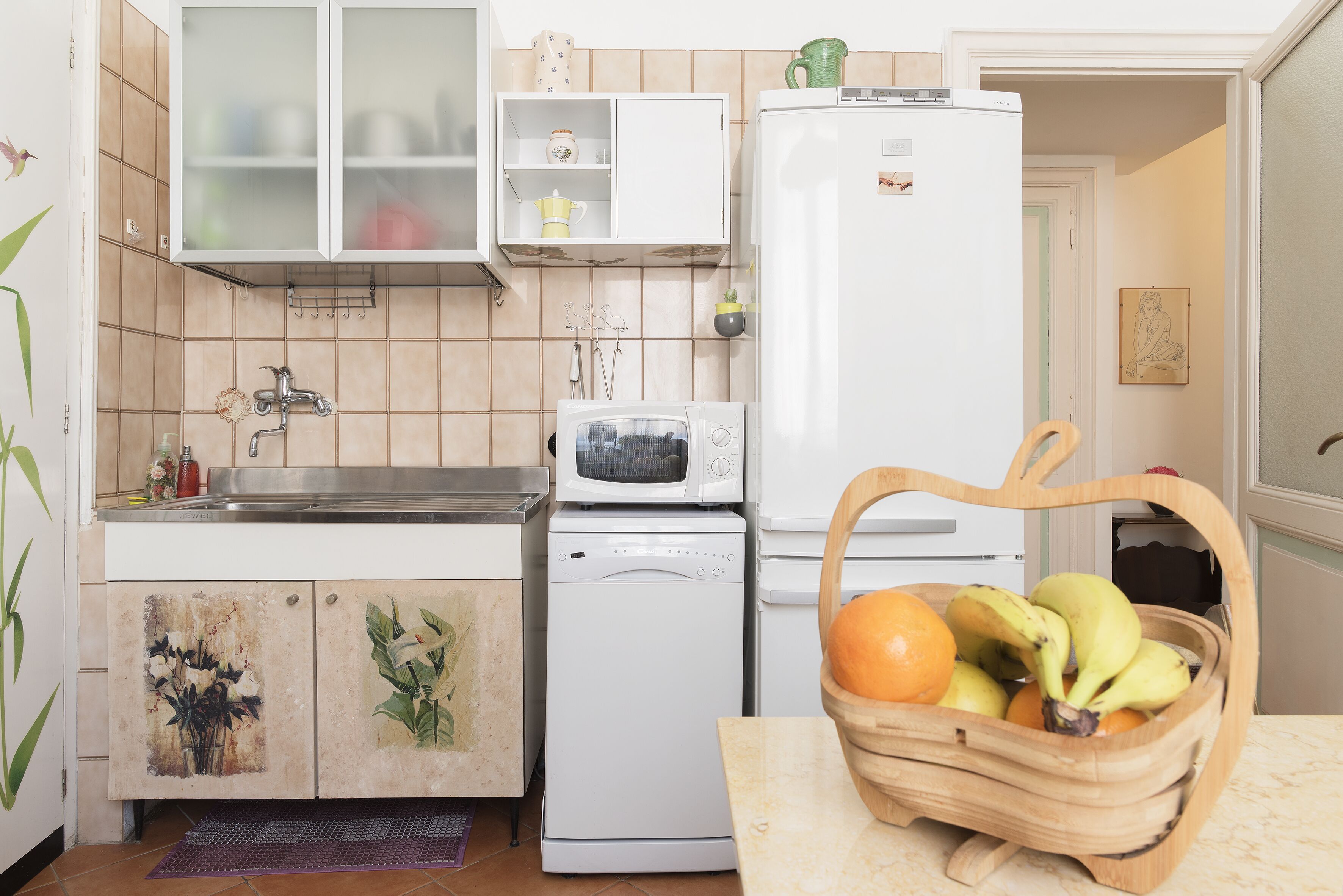 Une cuisine équipée d’un four à micro-ondes, d’un lave-vaisselle et d’un panier de fruits posé sur le plan de travail.