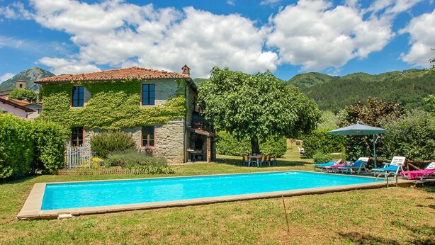 A swimming pool with a stone house in the background, surrounded by greenery and mountains. - House with private pool at 2,8 km from Castiglione di Garfagnana. Panoramic view (villa collemandina)