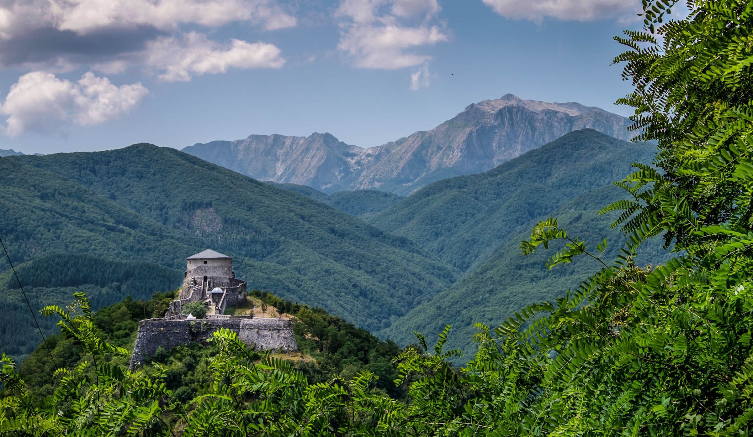 A historical stone structure with a dome, surrounded by lush green hills and mountains.