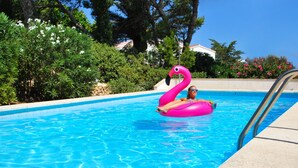Een zwembad met helderblauw water, omringd door weelderige begroeiing en een roze flamingo drijvend object.