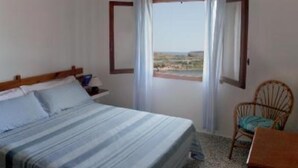 Een slaapkamer met een bed, een stoel, een raam met gordijnen en uitzicht op het landschap.