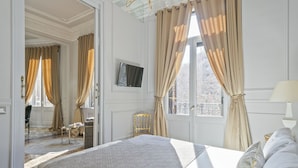 Habitación de hotel con una cama grande, un televisor montado en la pared y vistas de la ciudad a través de las ventanas.