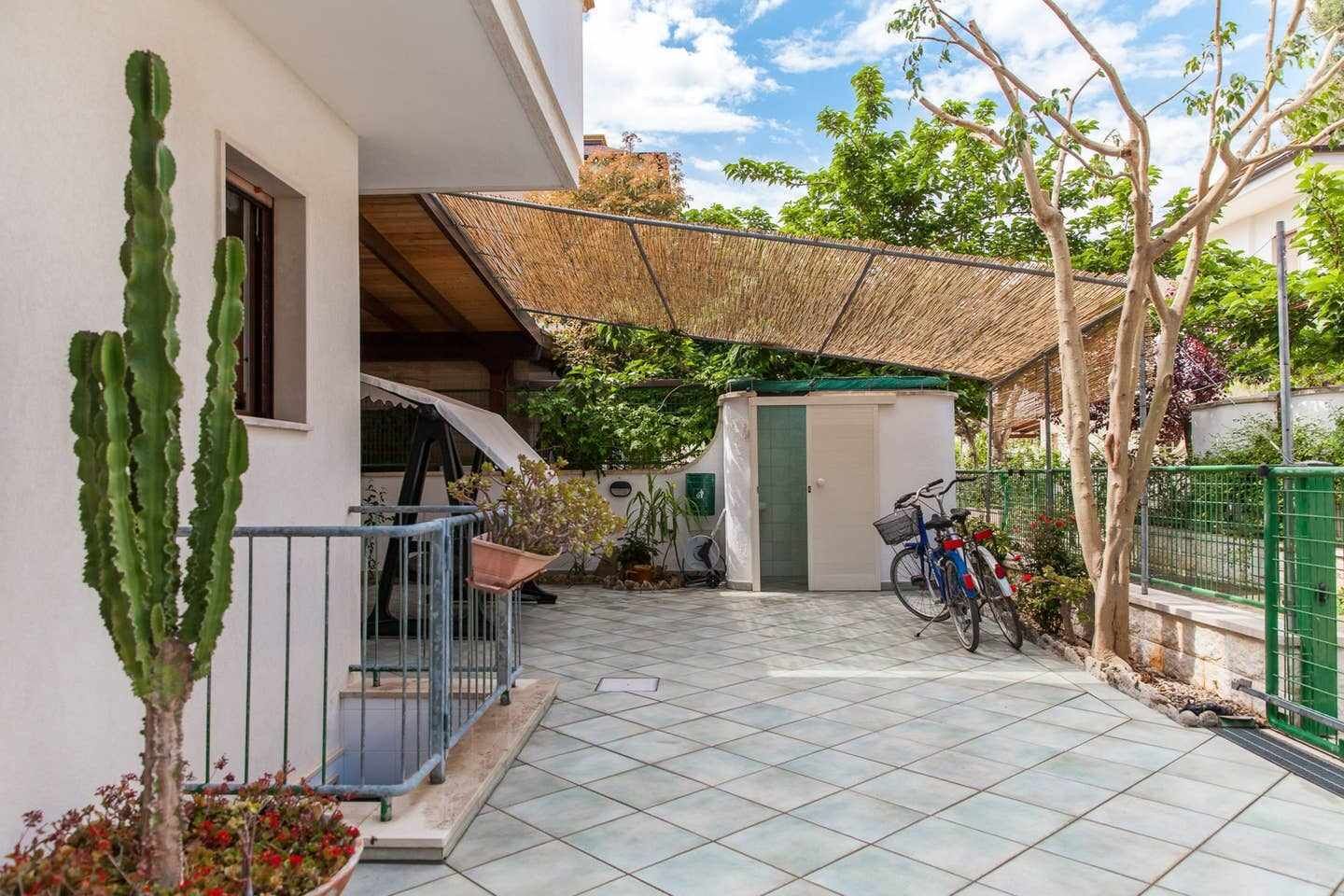 Un quartier résidentiel avec une terrasse carrelée, un cactus, un vélo et un petit abri de jardin.