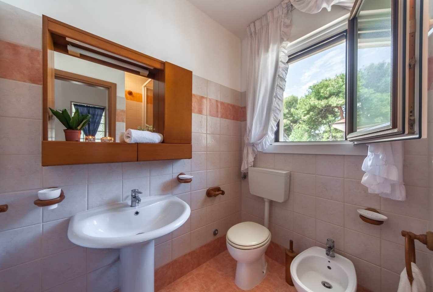 Ein Badezimmer mit Waschbecken, Toilette, Bidet und einem Fenster mit Vorhängen.